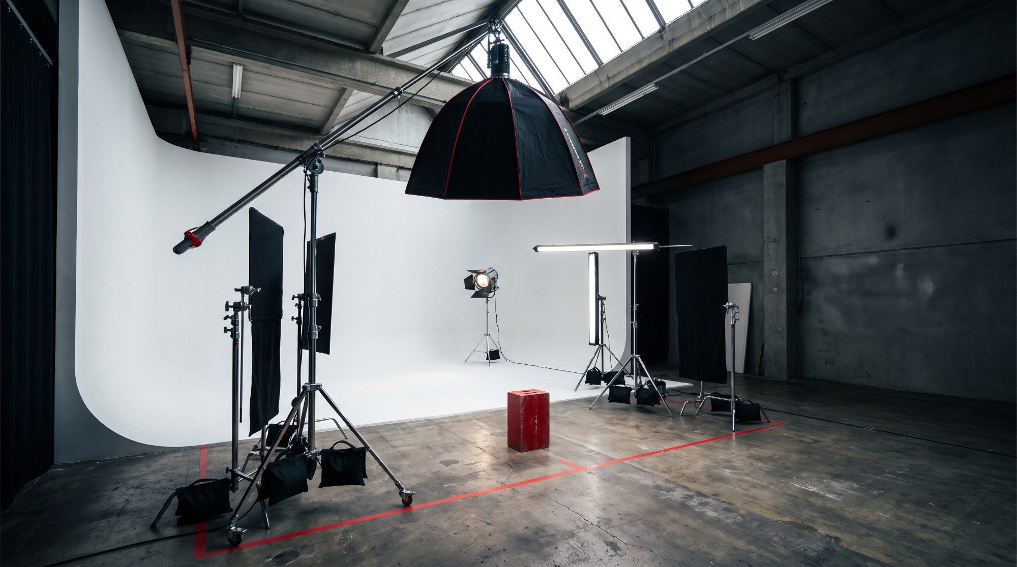 An empty professional studio set with a boom-mounted octabox overhead, a separate background light aimed at a white cyclorama from a distance, and a taped camera line on the floor